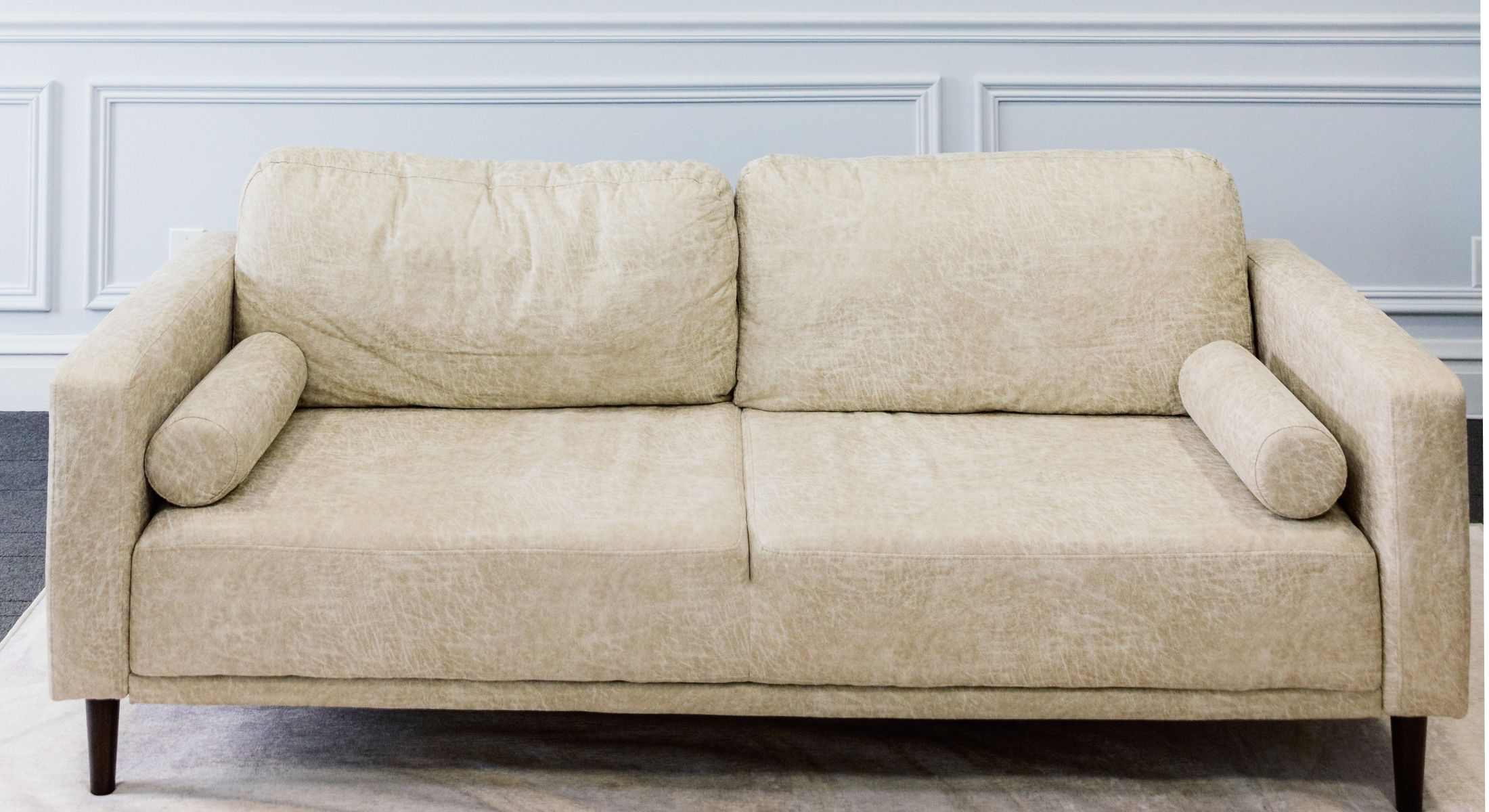 Beige loveseat with cylindrical cushions on arms.