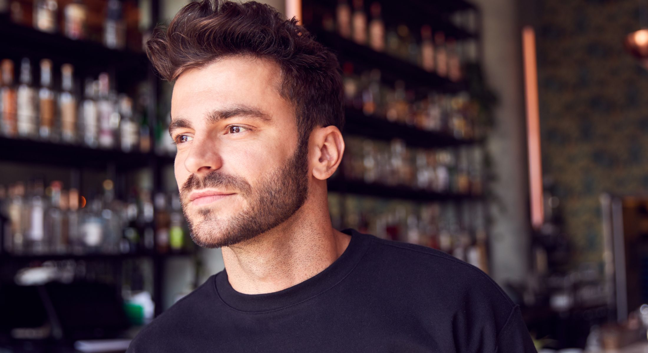 Hinsdale hair rejuvenation model in black shirt looking thoughtfully at bar.